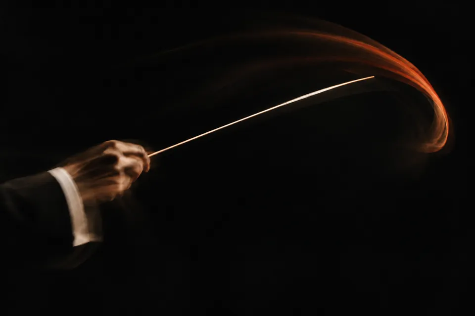 A conductor's baton sweeping through the dark, trailing warm light